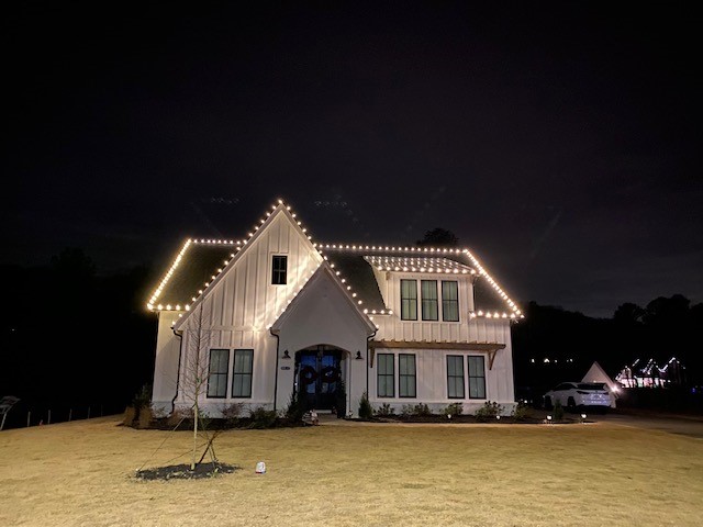 New construction home with warm holiday lighting across the front elevation